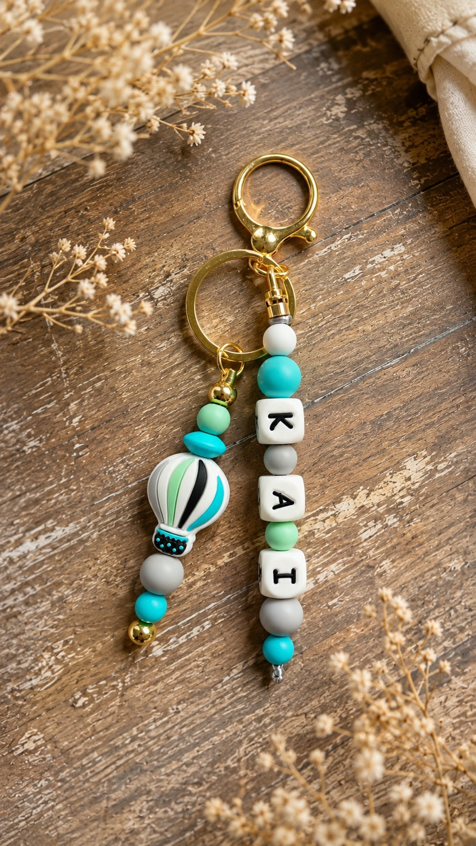 Personalised beaded keychain in turquoise, mint, white and gold hanging from a neutral sports bag outdoors.
