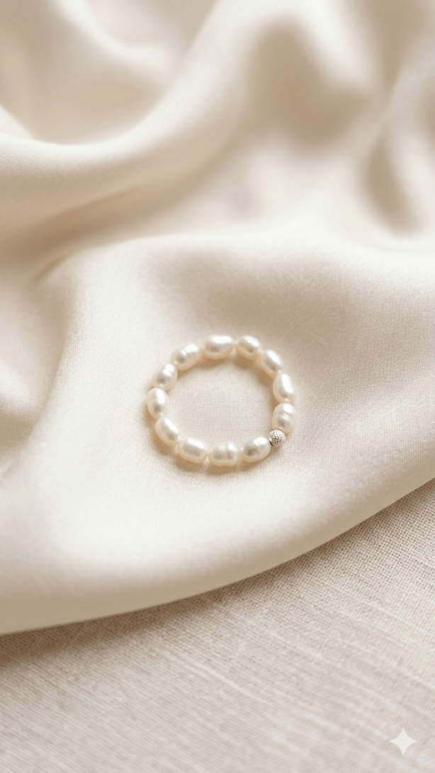 A woman’s hand wearing a delicate, handmade elastic pearl ring styled casually with a simple t-shirt, showing how perfectly the stretch design fits the finger.