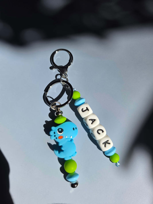 Personalised boy's backpack name tag made of colourful BPA-free silicone beads with a sturdy metal clasp, attached to a school bag zipper as a custom identifier.