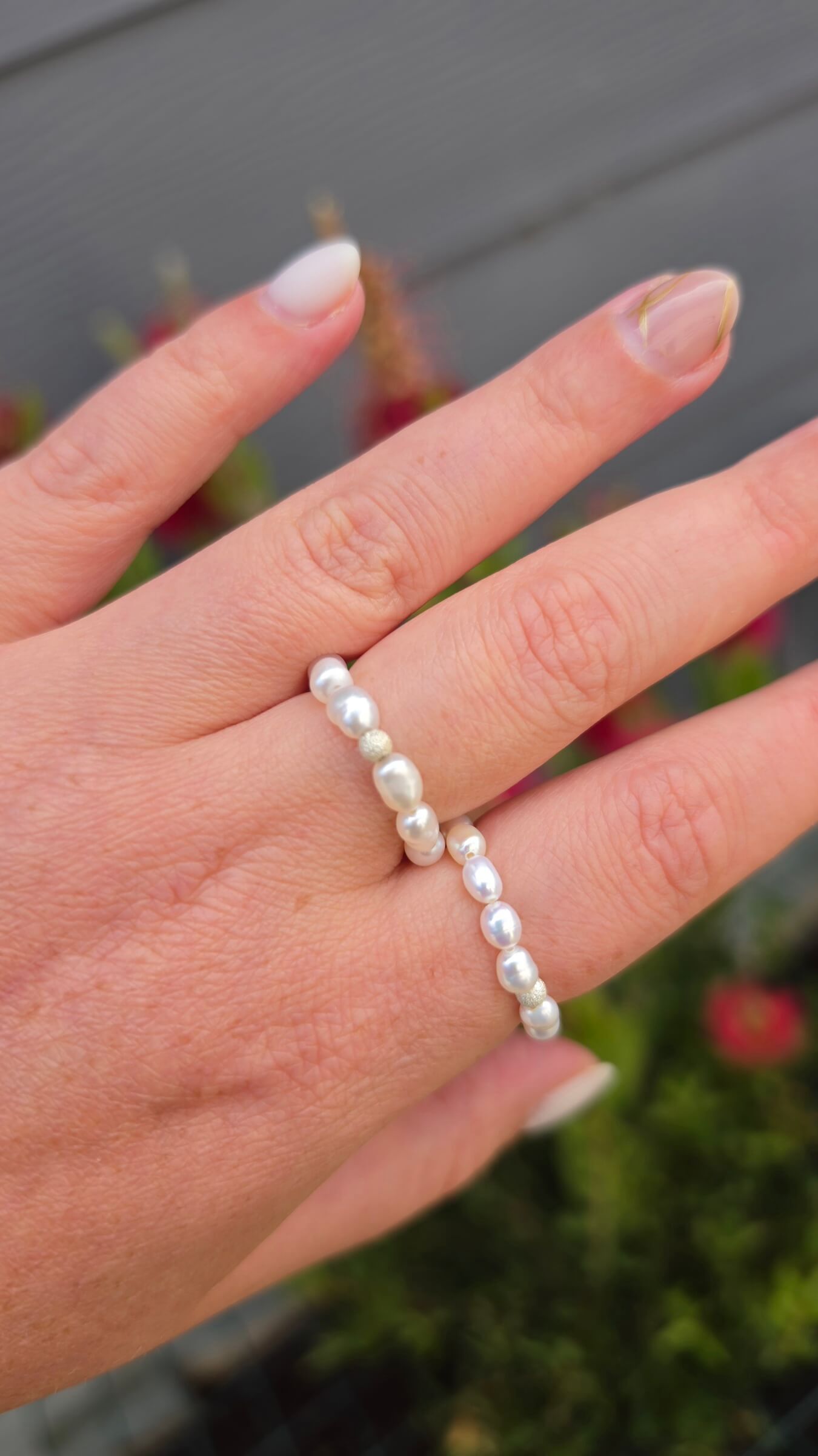 A stack of two delicate rice pearl elastic rings in sizes 3-4mm and 4-5mm on a model's finger, creating a beautiful, cascading luxury jewelry effect.