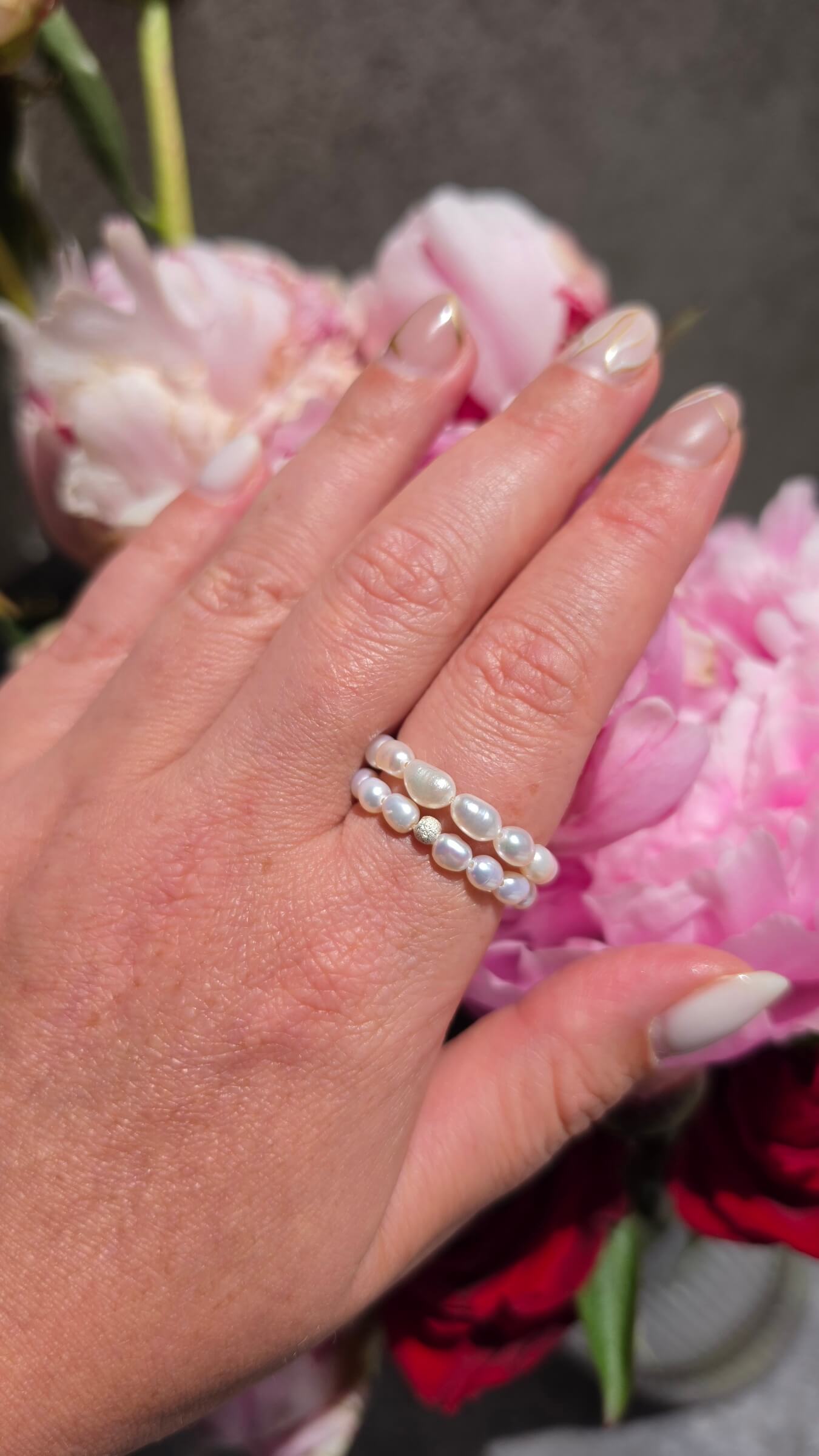 A woman’s hand wearing a delicate, handmade elastic pearl ring styled casually with a simple t-shirt, showing how perfectly the stretch design fits the finger.