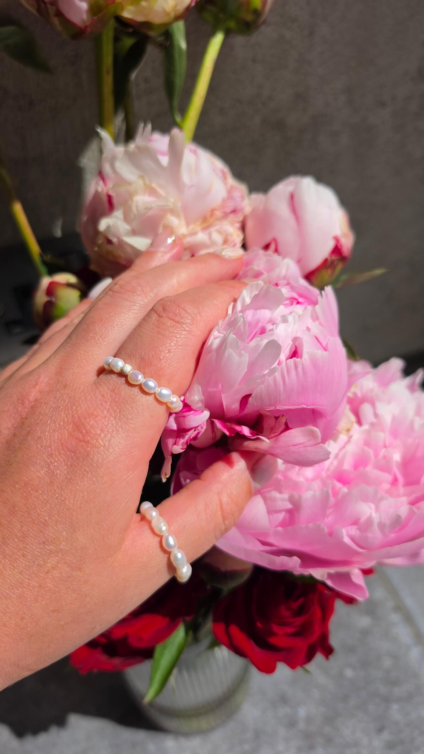 A woman’s hand wearing a delicate, handmade elastic pearl ring styled casually with a simple t-shirt, showing how perfectly the stretch design fits the finger.