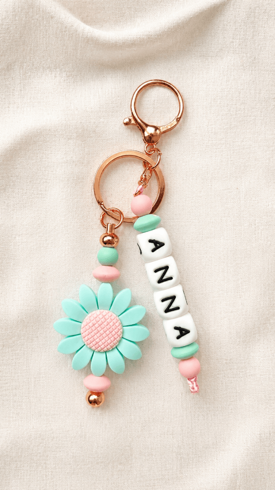 Product on linen background
Personalised silicone bag charm with custom name letter beads, pastel pink and mint beads, rose-gold hardware and daisy flower charm displayed on a soft neutral linen background.