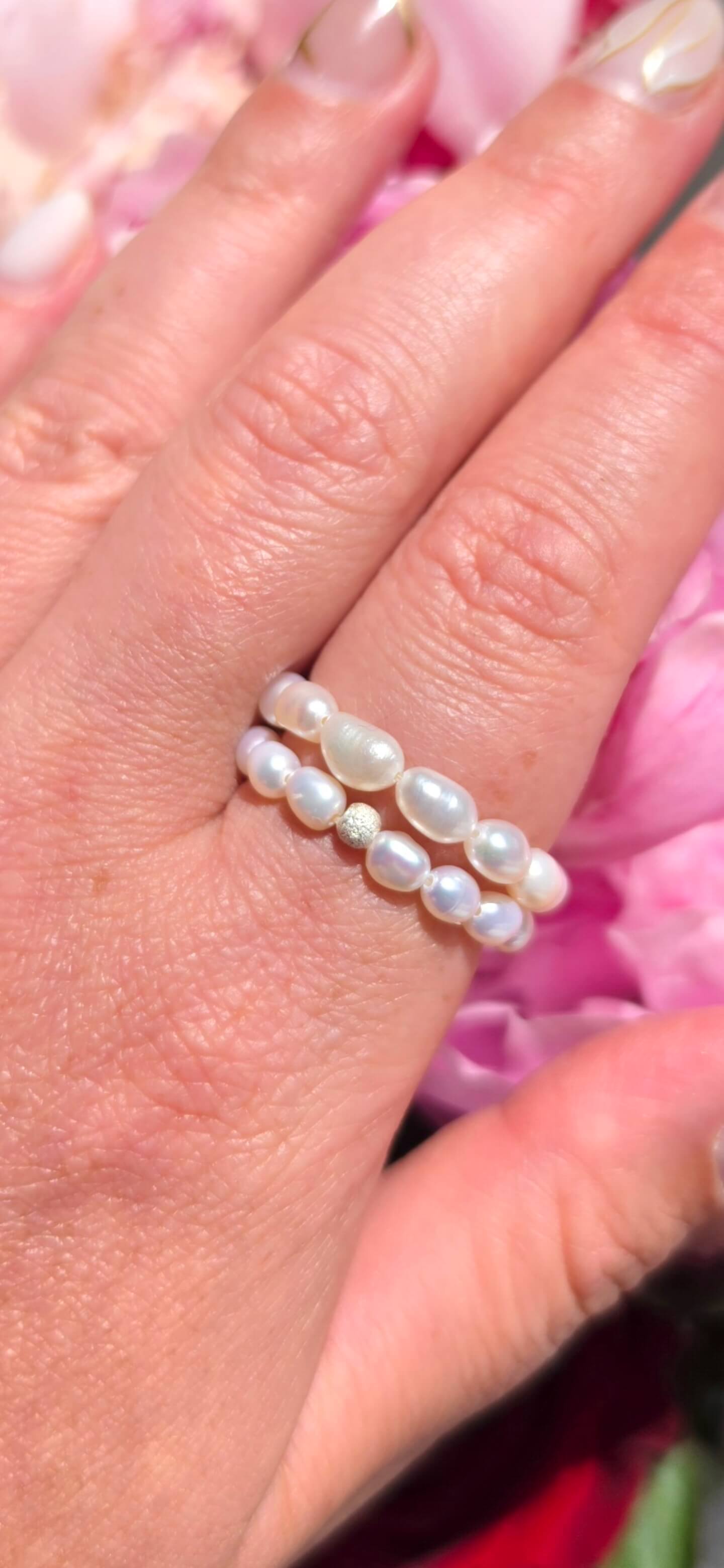 A close-up shot of the Timeless Rice Pearl Elastic Ring, featuring genuine, lustrous white rice-shaped freshwater pearls and a sparkling diamond-cut 925 sterling silver bead.