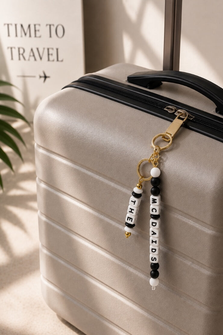 Personalised black and white silicone bead luggage tag with gold-tone hardware attached to a suitcase, custom family name travel accessory.
