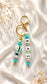 Turquoise and mint beaded keyring with personalised letter beads displayed on a neutral sports duffel bag in an outdoor setting.