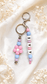 Elegant silicone bag charm with purple, blue and soft pink beads and silver-tone hardware on a soft cream background.