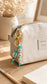Personalised beaded keychain in turquoise, mint, white and gold hanging from a neutral sports bag outdoors.
