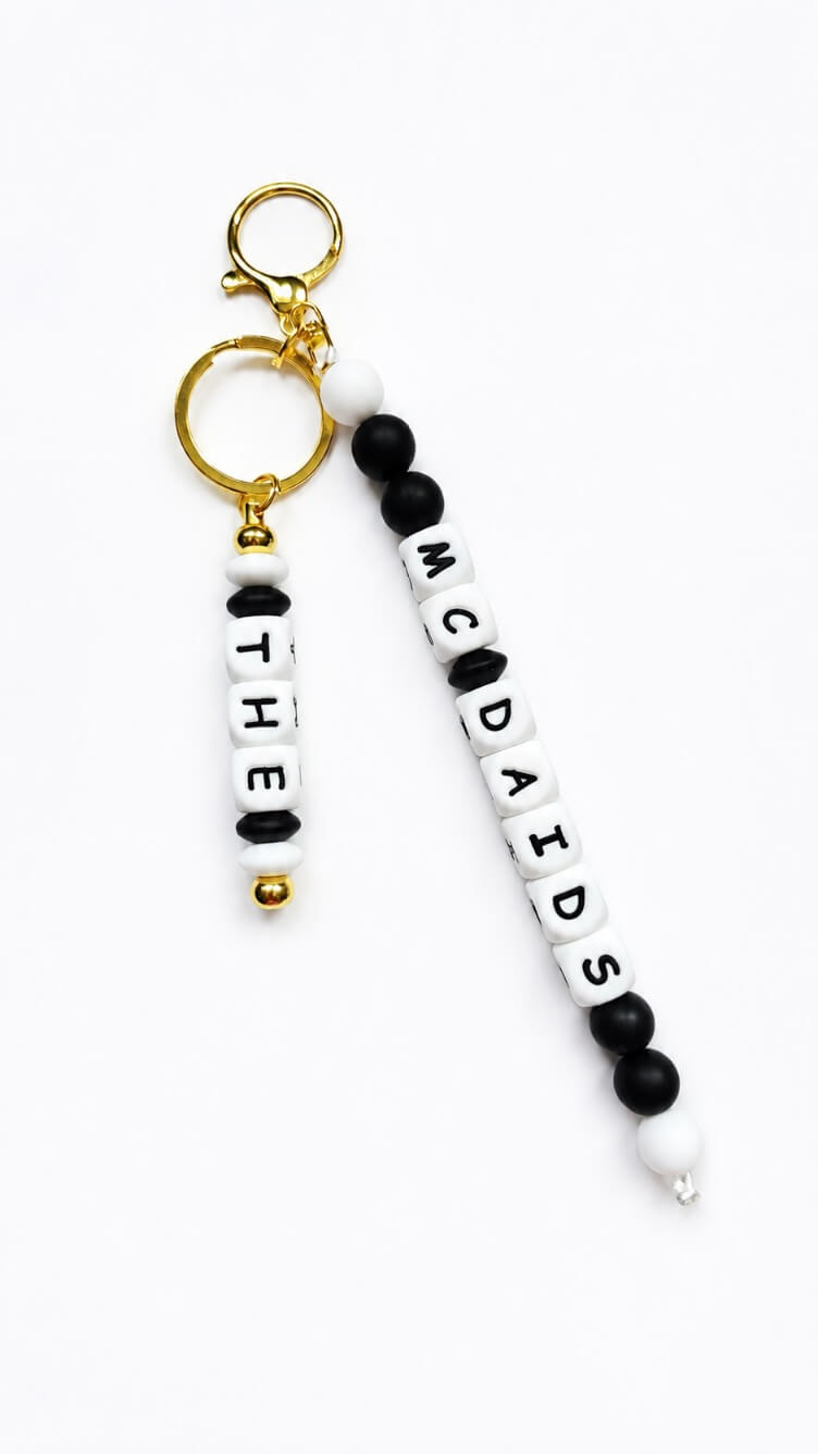 Close-up of a personalised luggage tag featuring soft matte silicone beads, white letter beads and elegant gold-tone metal rings.