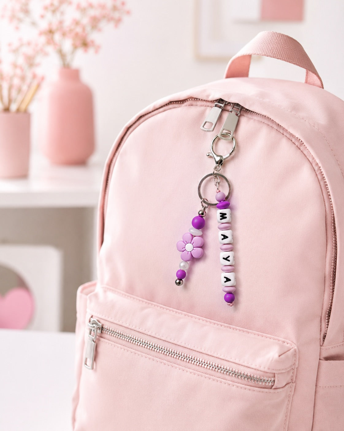 Personalised silicone backpack charm with custom name beads, pastel colours and flower detail, handmade in Ireland and attached to a school bag.

